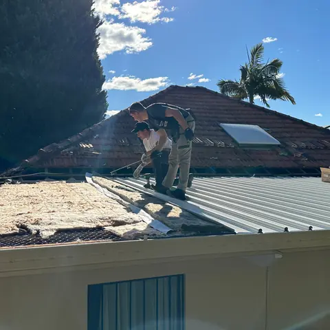 Two roofers working on a partially stripped residential roof