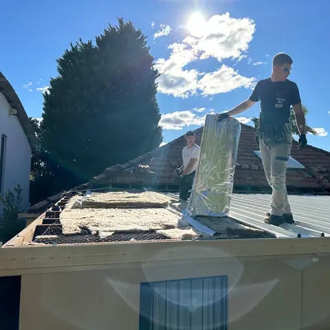 Roofer carrying roofing material across a partially stripped roof