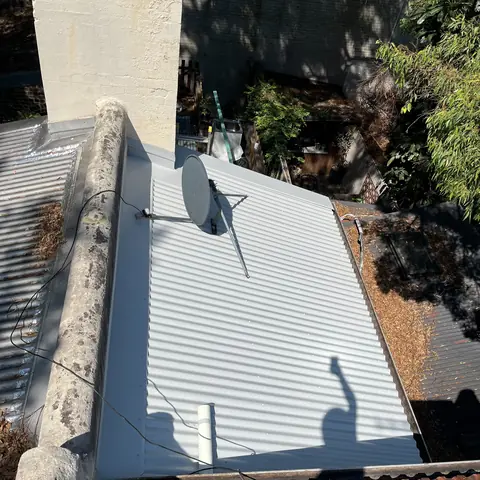 Light grey corrugated metal roof around a masonry chimney, viewed from above