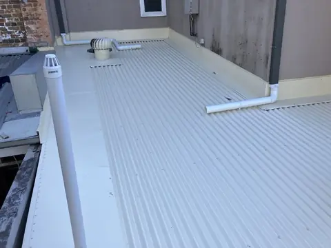 Light grey corrugated metal roof with a flue and roof vent